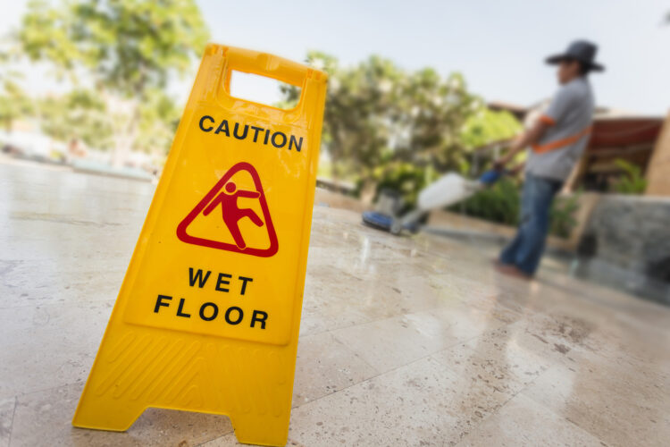 Why Slip And Fall Injuries Are Not Funny - Yellow caution sign and blur of man doing floor polishing