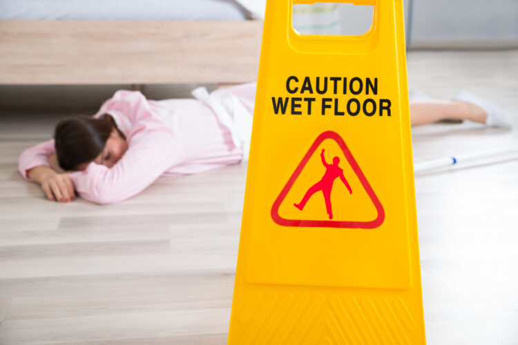 Slip And Fall Accidents: How To React - Wet Floor Sign With Fainted Housekeeper Lying On Floor
