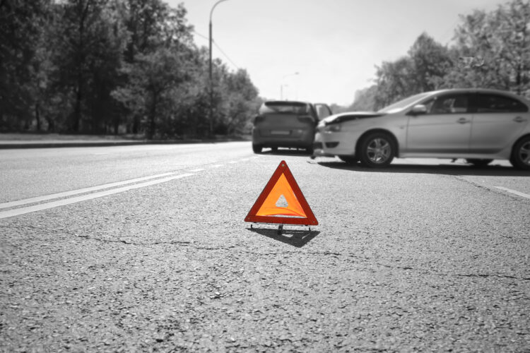Defensive Driving Tips & Accident Prevention - Hazard warning triangle laid out on the road behind two crashed cars, black and white photo with a red accent on a triangle